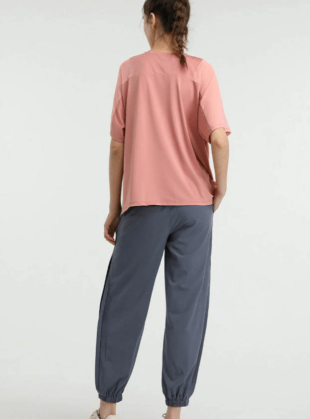 Woman wearing a loose pink mesh short sleeve running t-shirt paired with grey athletic pants, showcasing women's workout sports clothing.